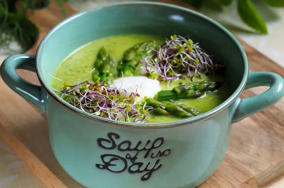 Aksamitna zupa z zielonych szparagów, udekorowana kiełkami i kleksem śmietany, w ceramicznej misce z napisem "Soup of the Day".