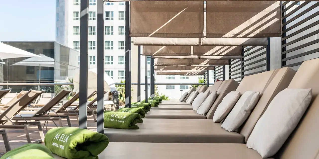 Tumbonas listas para el relax en la terraza del Meliá Valencia, con toallas verdes y vistas a la ciudad.
