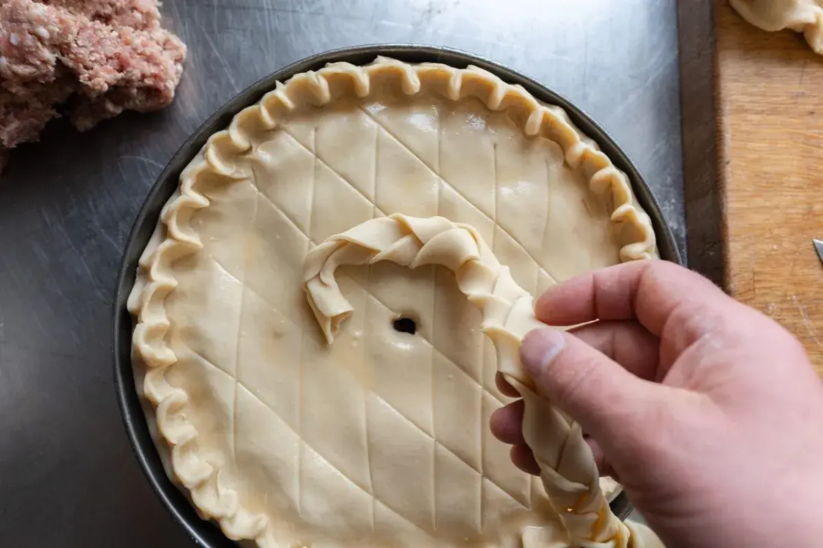 Préparation d'une tarte salée, peut-être une recette joue de porc rapide. Une pâte est décorée avec une tresse.
