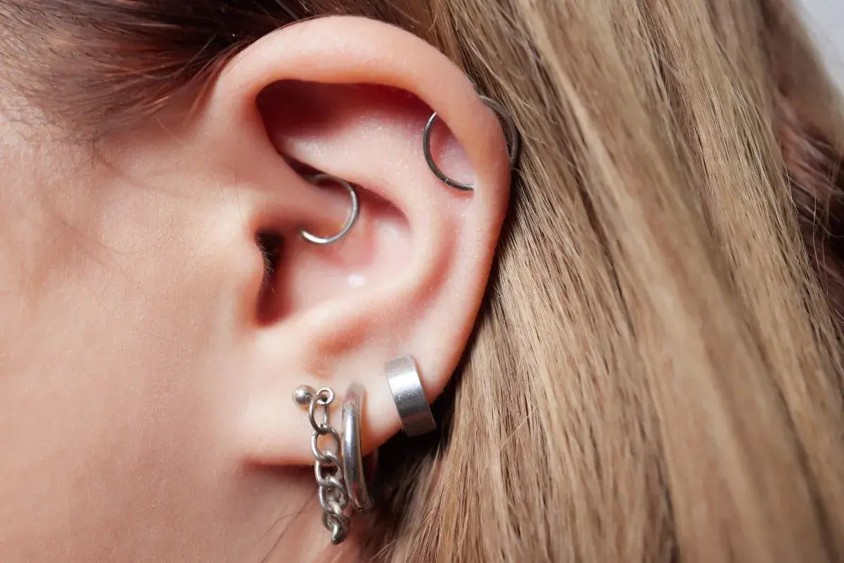 Ucho z kilkoma kolczykami, w tym daith piercing z małym kółkiem.
