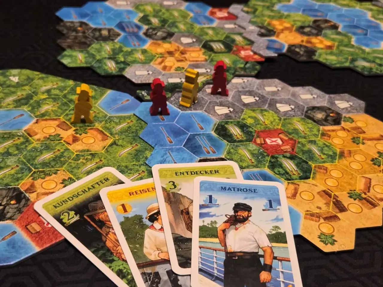 Spielbrett mit Figuren und Karten. Ein Seemann, Entdecker und andere Charaktere sind auf den Karten abgebildet. Ein spannendes Spiel für alle, die gute Brettspiele lieben.