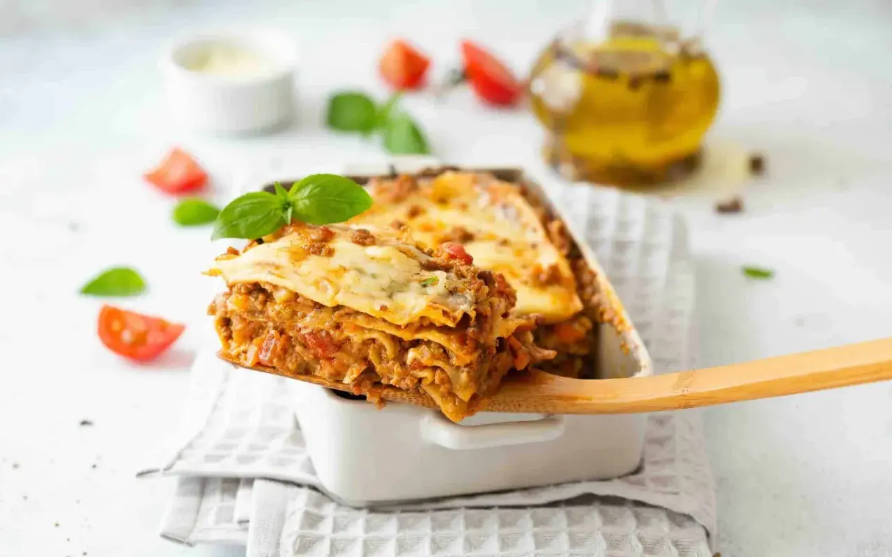 Une part généreuse de lasagne, digne d'une recette de chef italien, est servie. Tomates et basilic frais décorent ce plat réconfortant.
