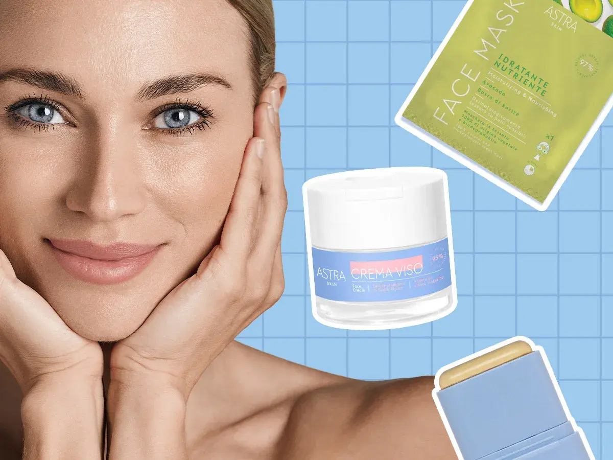 Donna con mani sul viso, circondata da prodotti Astra per la cura della pelle, per una skin longevity radiosa.