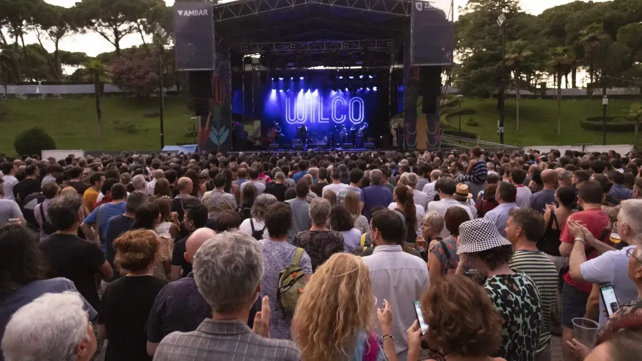 Gran concierto de Wilco en el **jardín de invierno Zaragoza**. Multitud disfruta al aire libre bajo un cielo crepuscular.