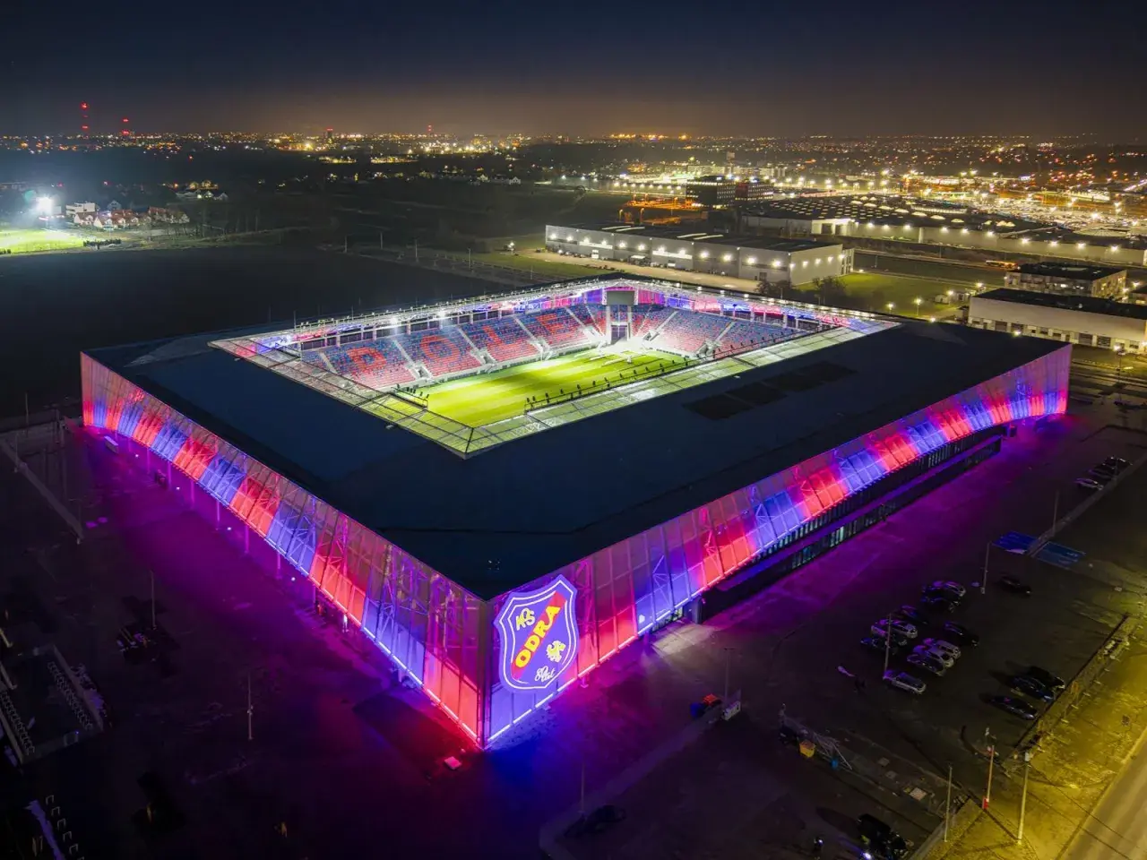 Nowoczesny stadion Odra Opole nocą, oświetlony na czerwono i niebiesko.