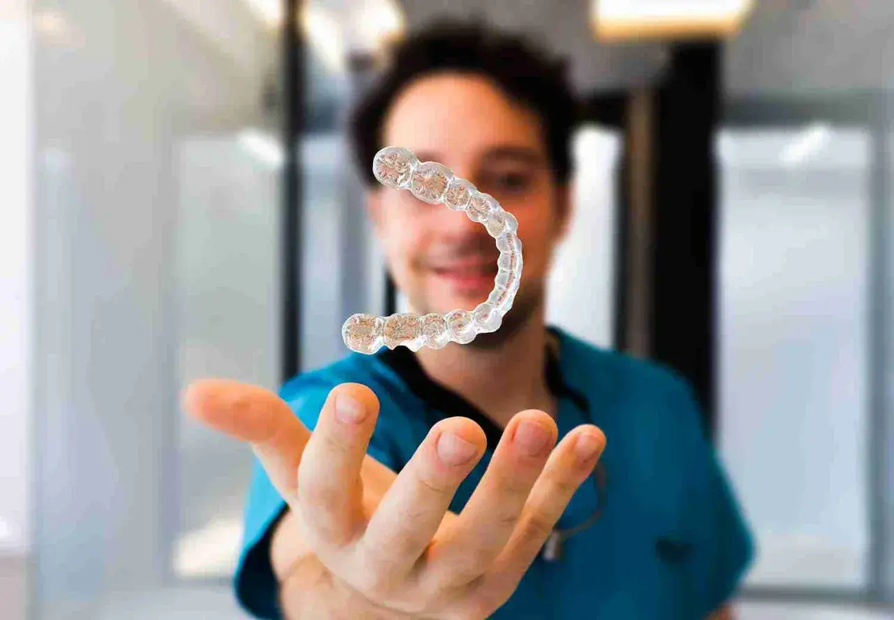 Un dentista sonriente muestra un alineador invisible, explicando cómo funcionan los alineadores invisibles para corregir la sonrisa.