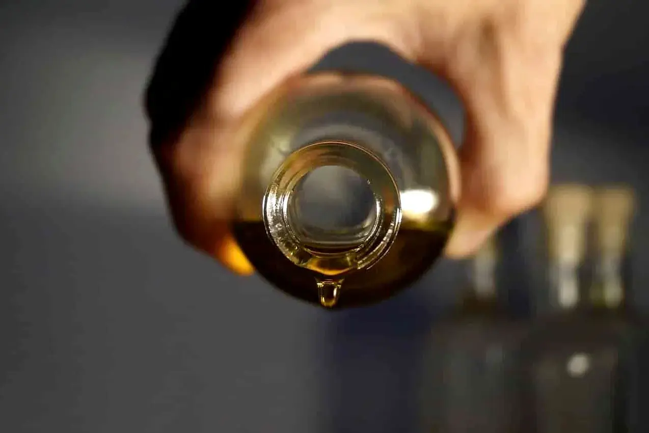 Une goutte d'huile dorée tombe d'une bouteille, parfait pour votre huile cheveux maison.