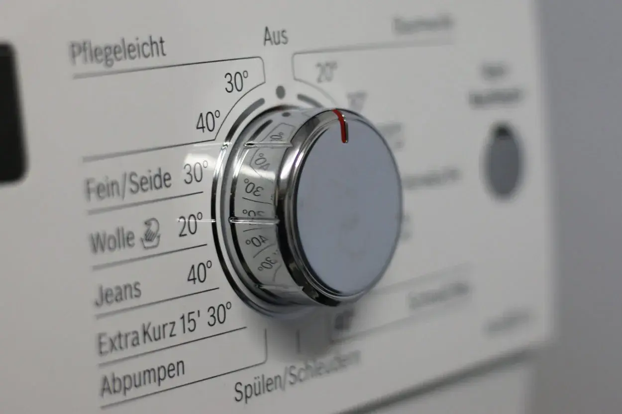 Drehknopf einer Waschmaschine mit verschiedenen Waschprogrammen wie Pflegeleicht, Fein/Seide, Wolle und Jeans.