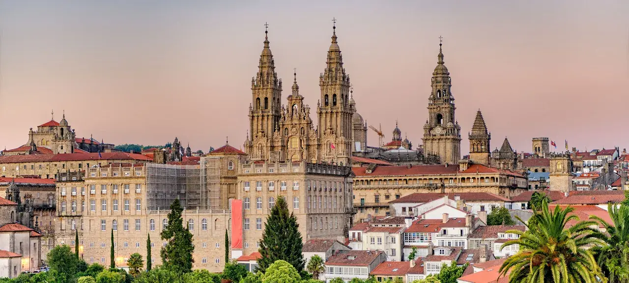 Majestatyczna katedra w Santiago de Compostela góruje nad miastem. W tle widać budynki i palmy.