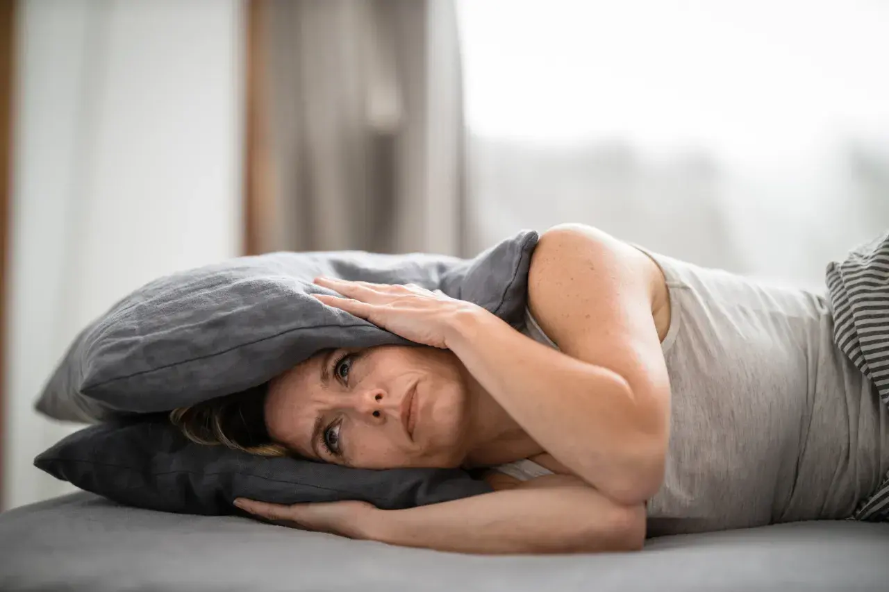 Frau mit Kissen über dem Kopf, die unter Tinnitus leidet und nach Linderung durch Osteopathie sucht.