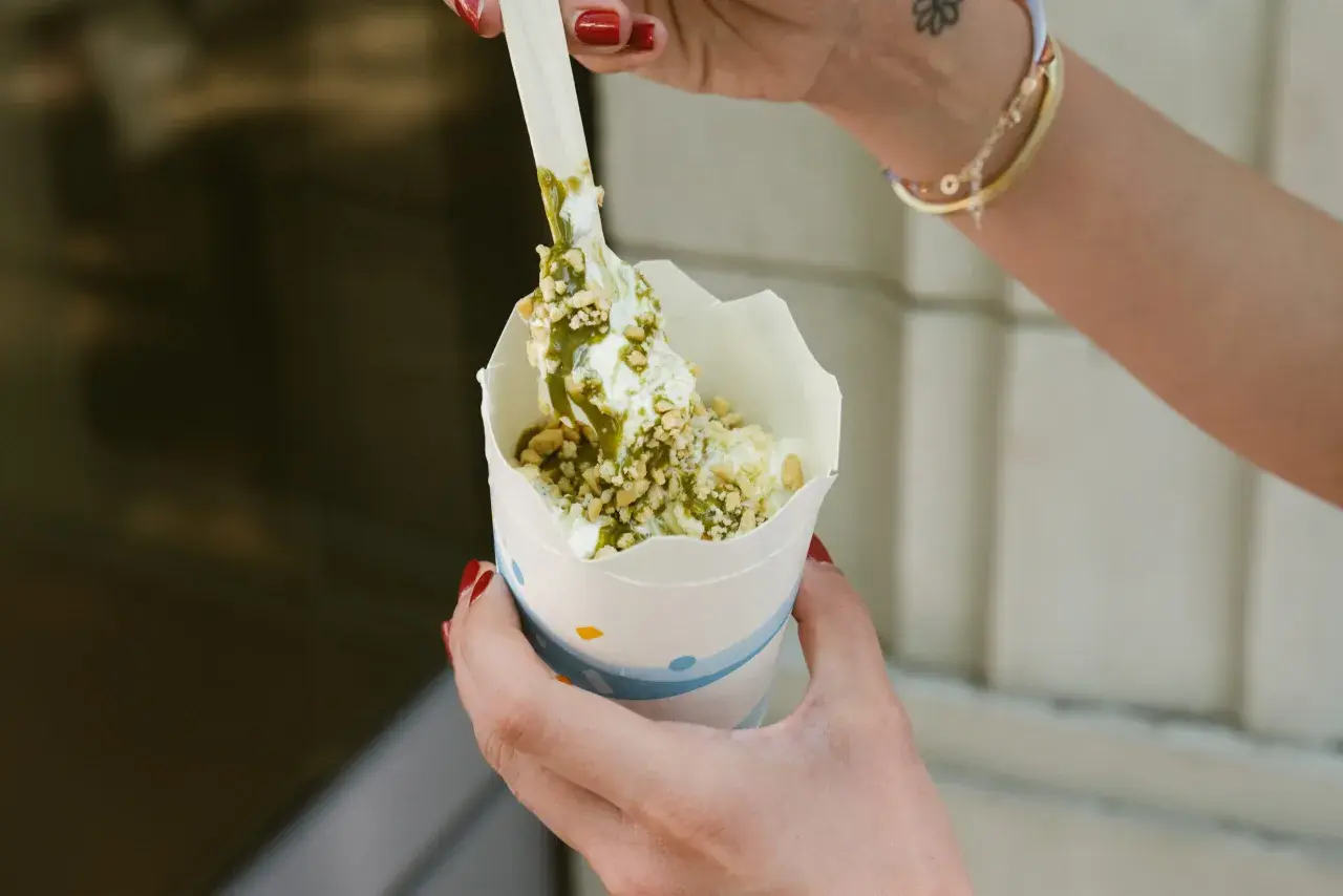 Ręce trzymają kubek z lodami mcflurry pistacjowe, posypane orzeszkami i polane zielonym sosem.