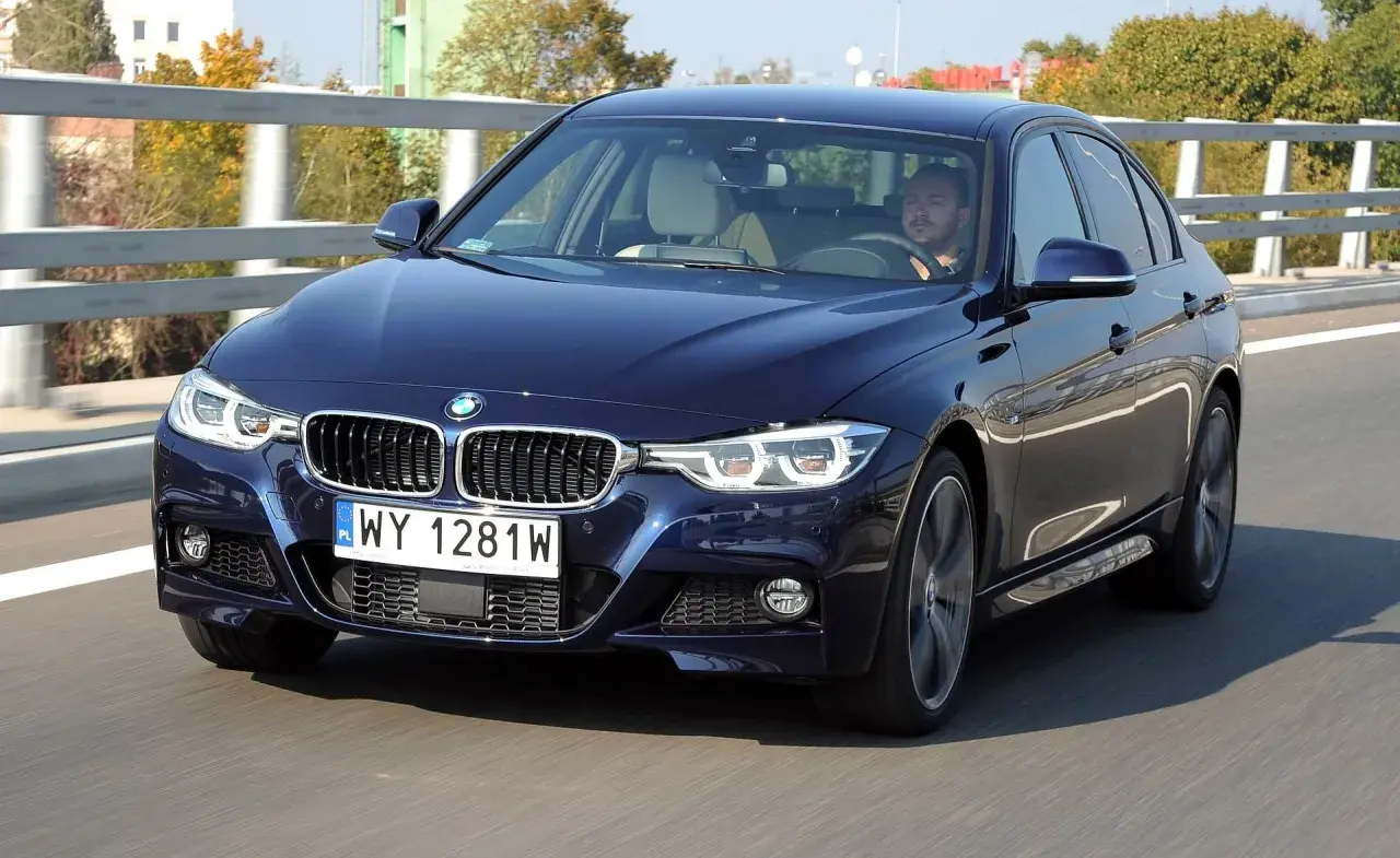 Ciemnoniebieskie BMW F30 M Pakiet pędzi po drodze. Kierowca skupiony na trasie.