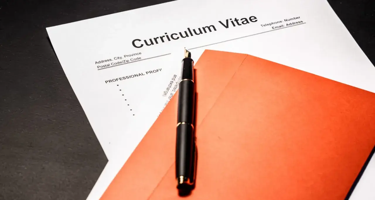 Eleganckie pióro na tle dokumentu Curriculum Vitae po angielsku i pomarańczowej koperty.