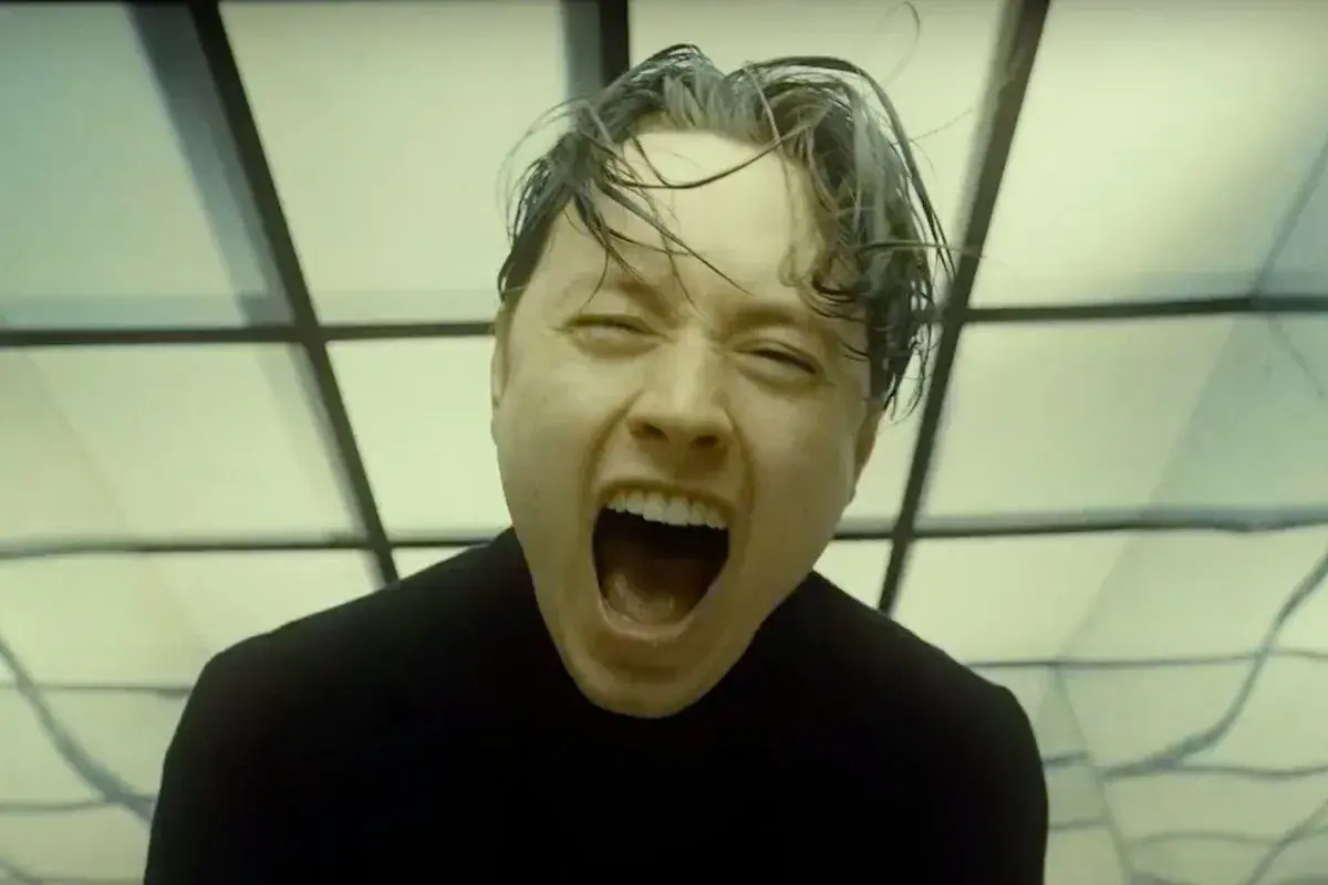 Noah Sebastian screams in a black shirt, his hair wet and messy, against a backdrop of geometric patterns.
