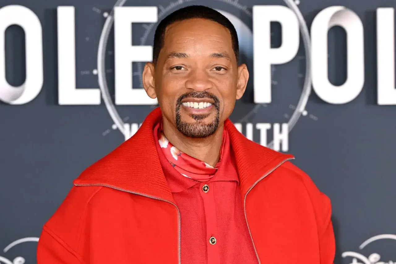 Will Smith, souriant, porte une veste rouge vif. On peut lire "POLE" en lettres blanches derrière lui, suggérant son prochain film.