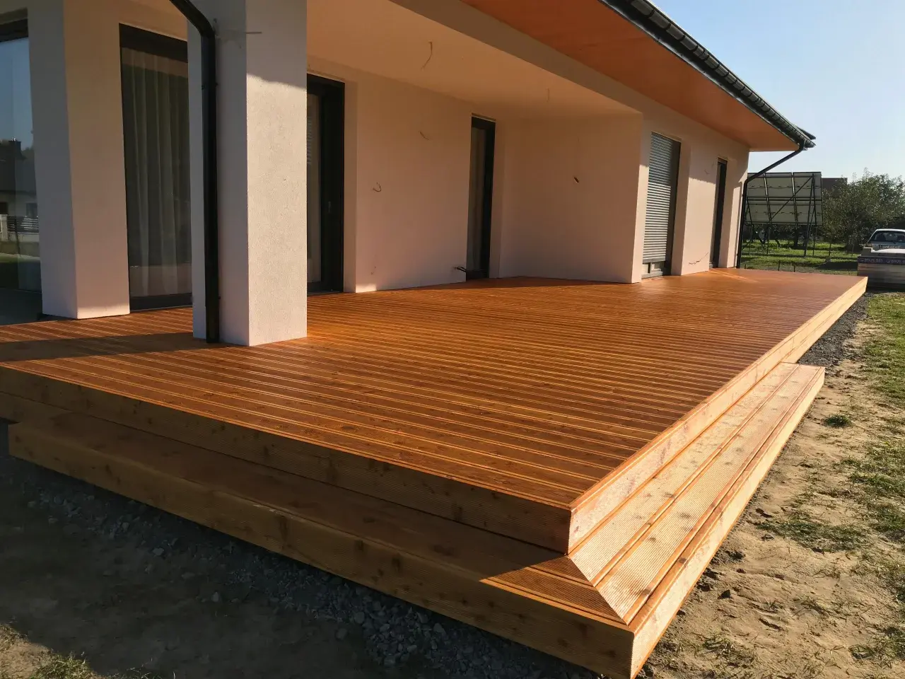 Nowa, drewniana terasa z widocznymi stopniami, zabezpieczona impregnatem do legarów tarasowych, lśni w słońcu.