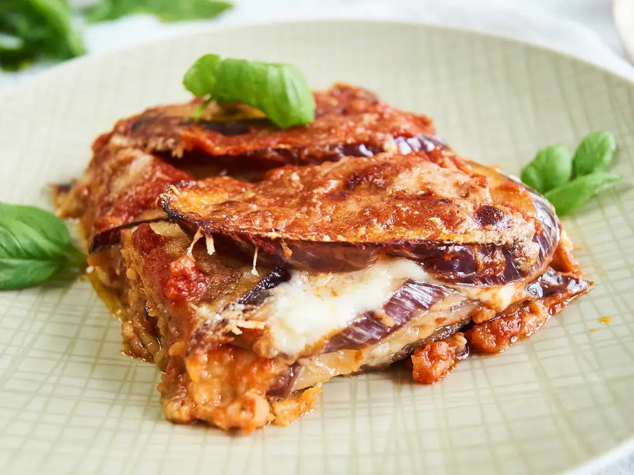 Parmigiana di Melanzane auf einem Teller mit Basilikum garniert.