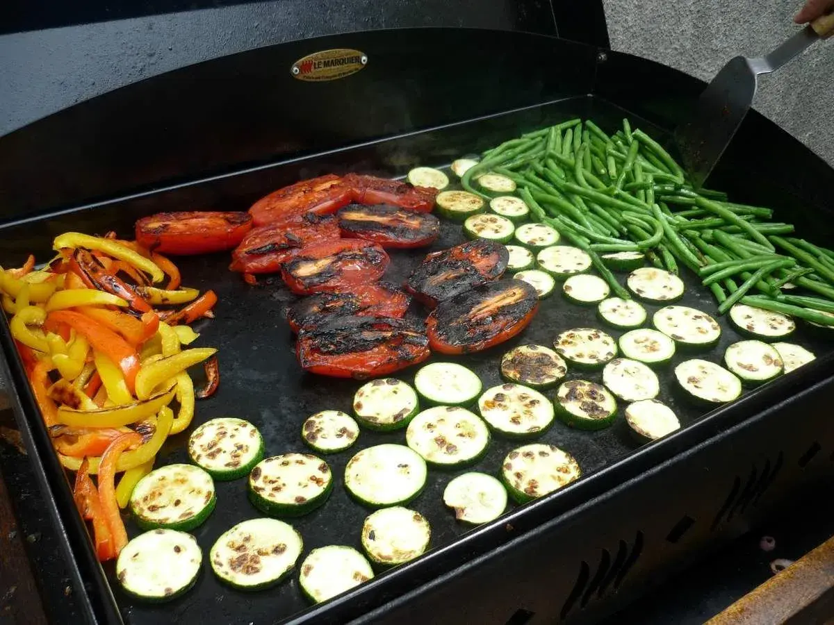 Poivrons, tomates, courgettes et haricots verts grillés sur une plancha. Une délicieuse pierrade végétarienne en préparation.