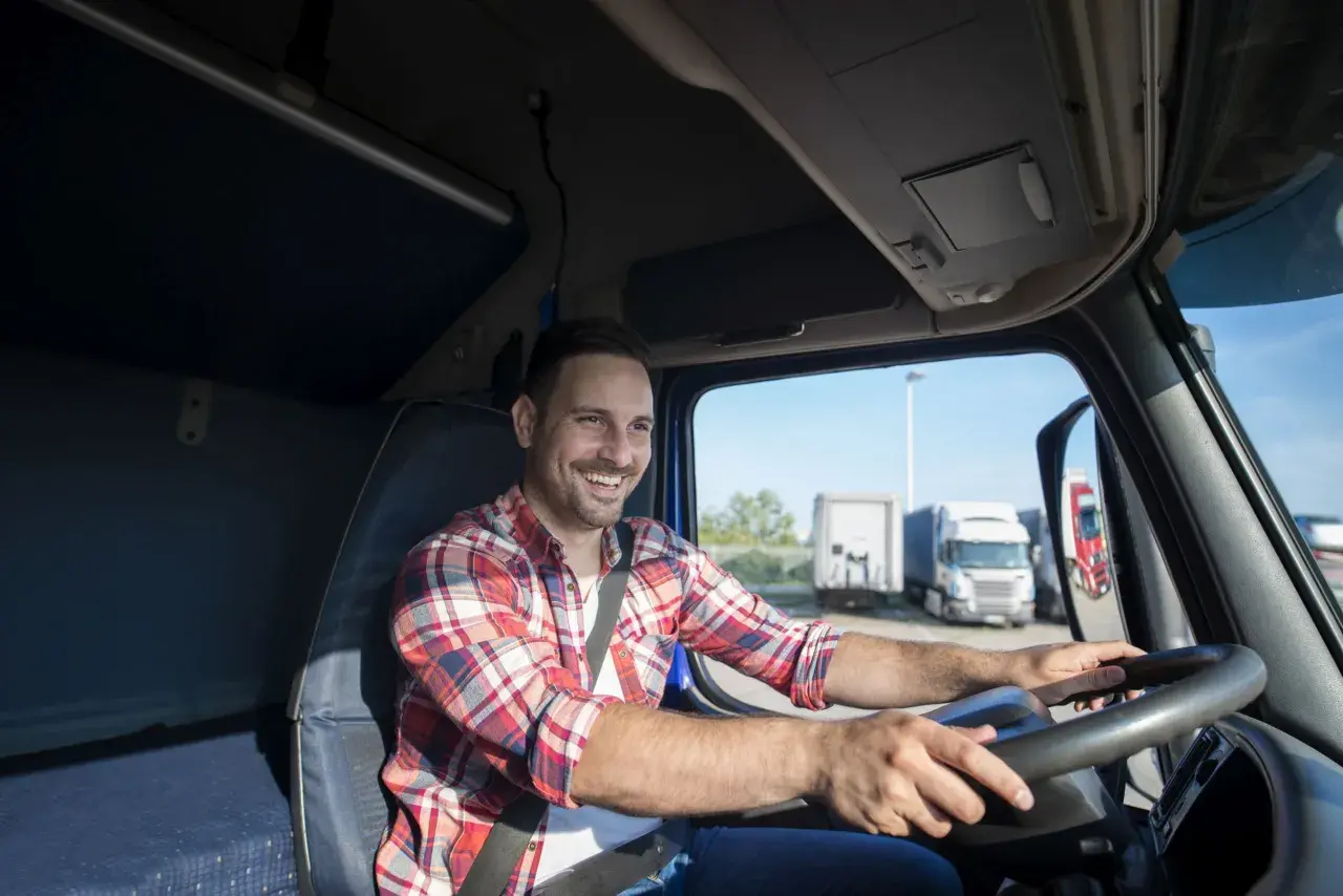 Uśmiechnięty kierowca w kratę za kierownicą ciężarówki. To jego dzień transportowca, gotowy na kolejną trasę.