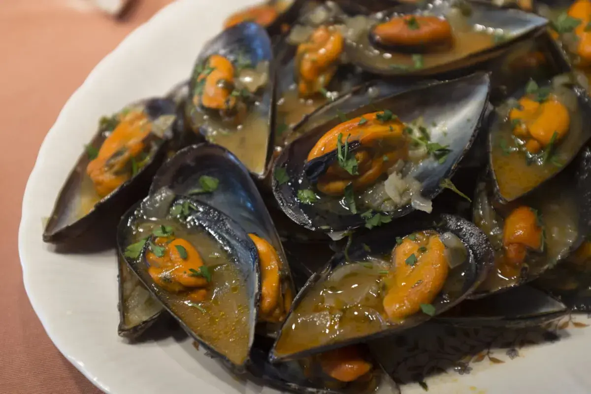 Un plato lleno de mejillones a la marinera, jugosos y con perejil picado, listos para disfrutar.