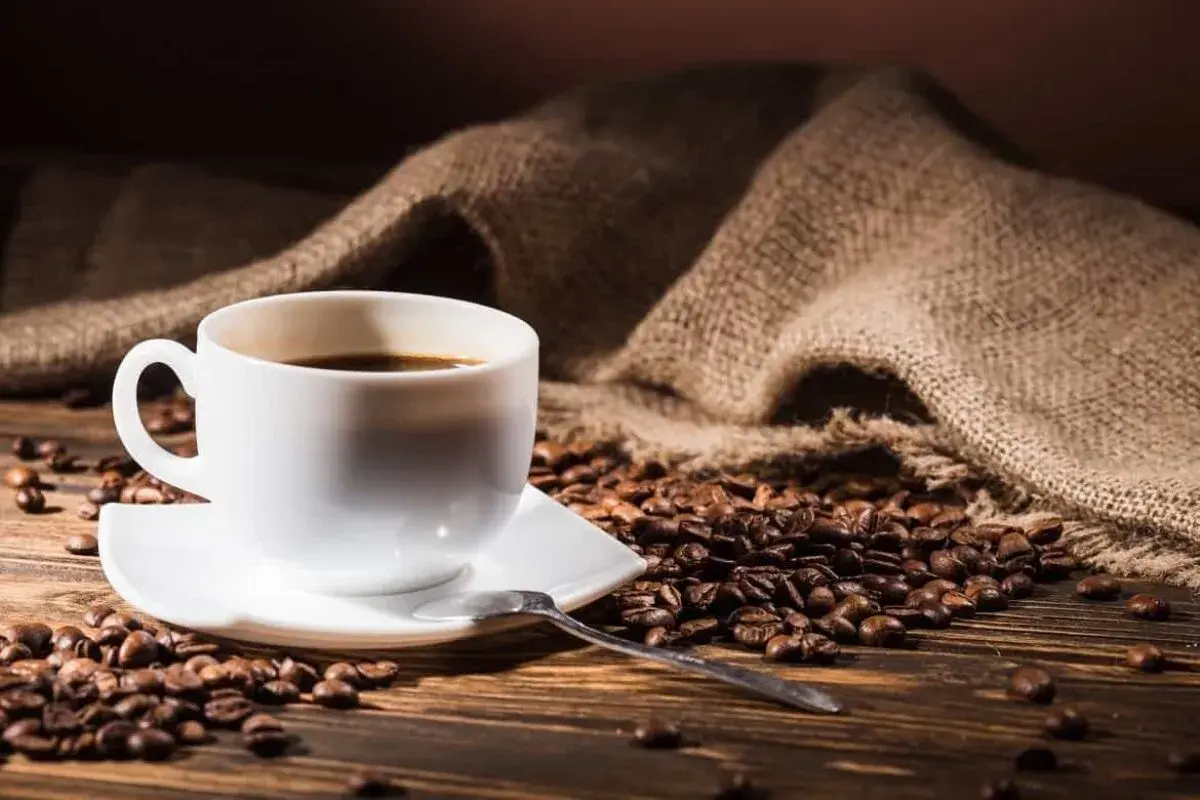 Aromatic espresso na drewnianym blacie, otoczone ziarnami kawy. Zastanawiasz się, ile kofeiny ma espresso?