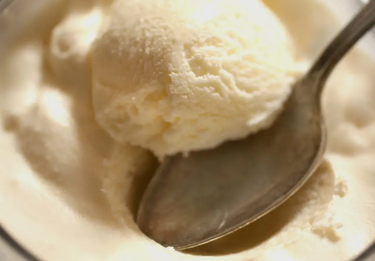 Kremowe lody z serka wiejskiego, idealne na deser. Łyżeczka zanurzona w słodkiej masie.