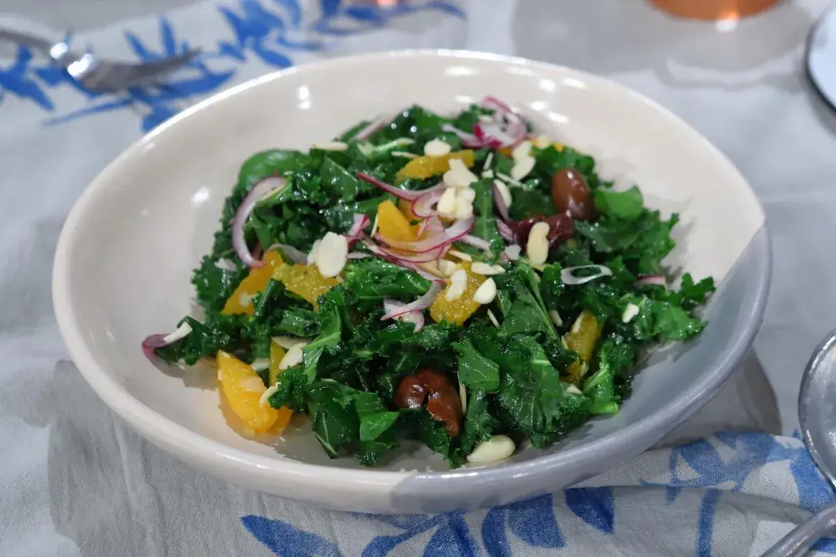 Ensalada siciliana vibrante con col rizada, gajos de naranja, cebolla morada, aceitunas y almendras laminadas.