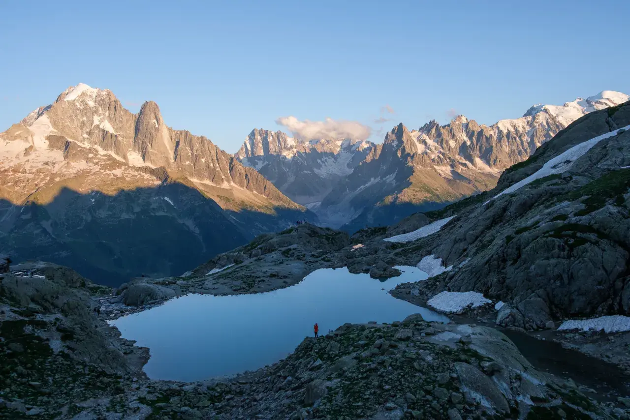 Un randonneur solitaire admire le reflet des Aiguilles Rouges dans un lac d'altitude. Le soleil couchant éclaire les sommets enneigés.