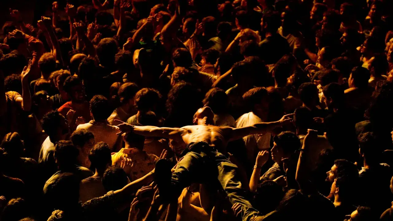 Tłum szaleje w moshpit, unosząc nagiego mężczyznę z rozłożonymi ramionami.