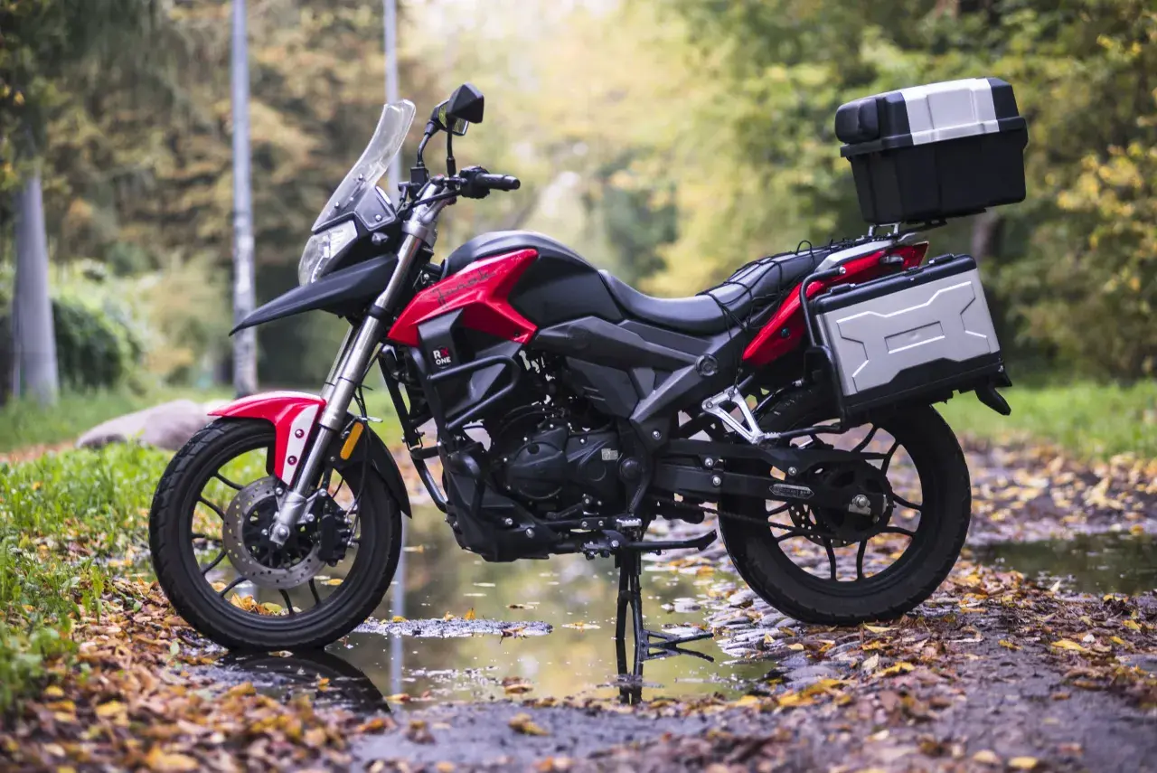 Czerwono-czarny motocykl szosowo turystyczny 125 z kuframi, gotowy na jesienne wyprawy po leśnej drodze.