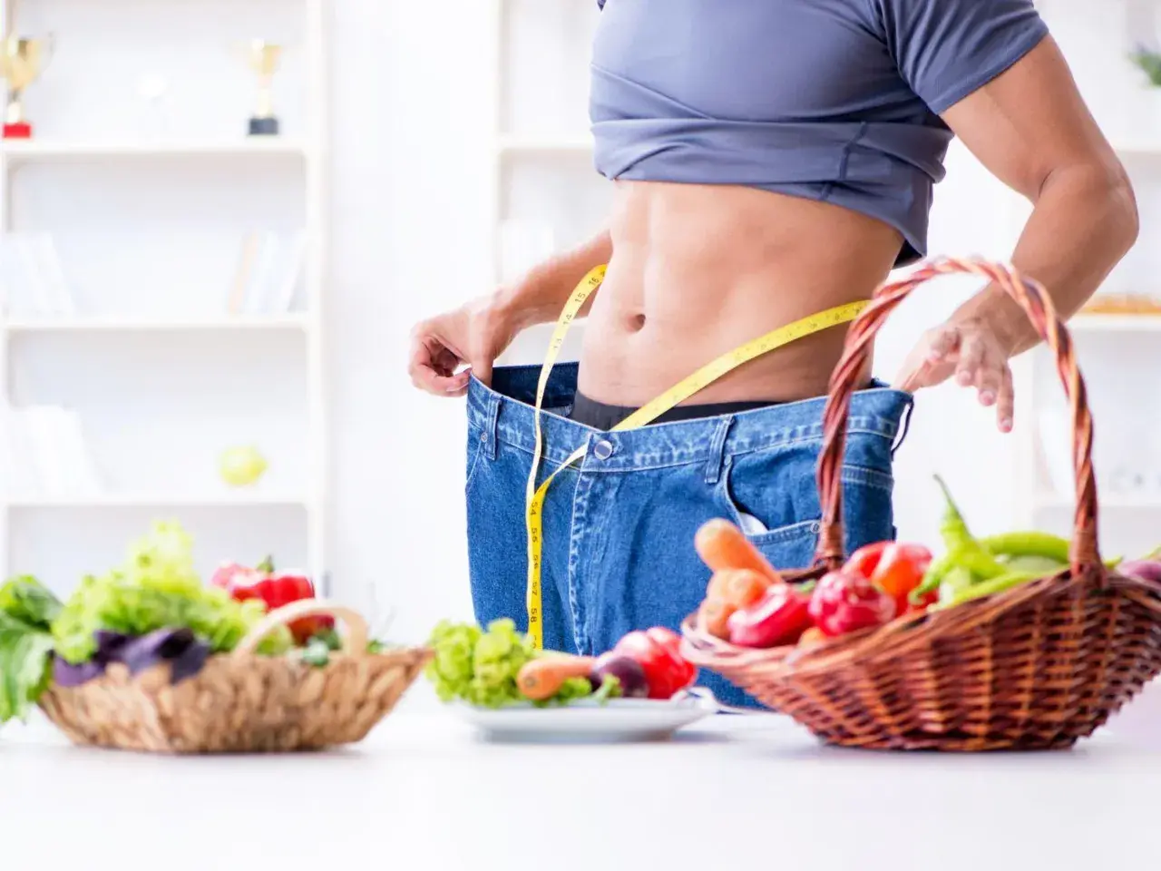 Uomo con jeans larghi e metro, simbolo di successo con dieta ipocalorica. Cesti di verdura fresca in primo piano.