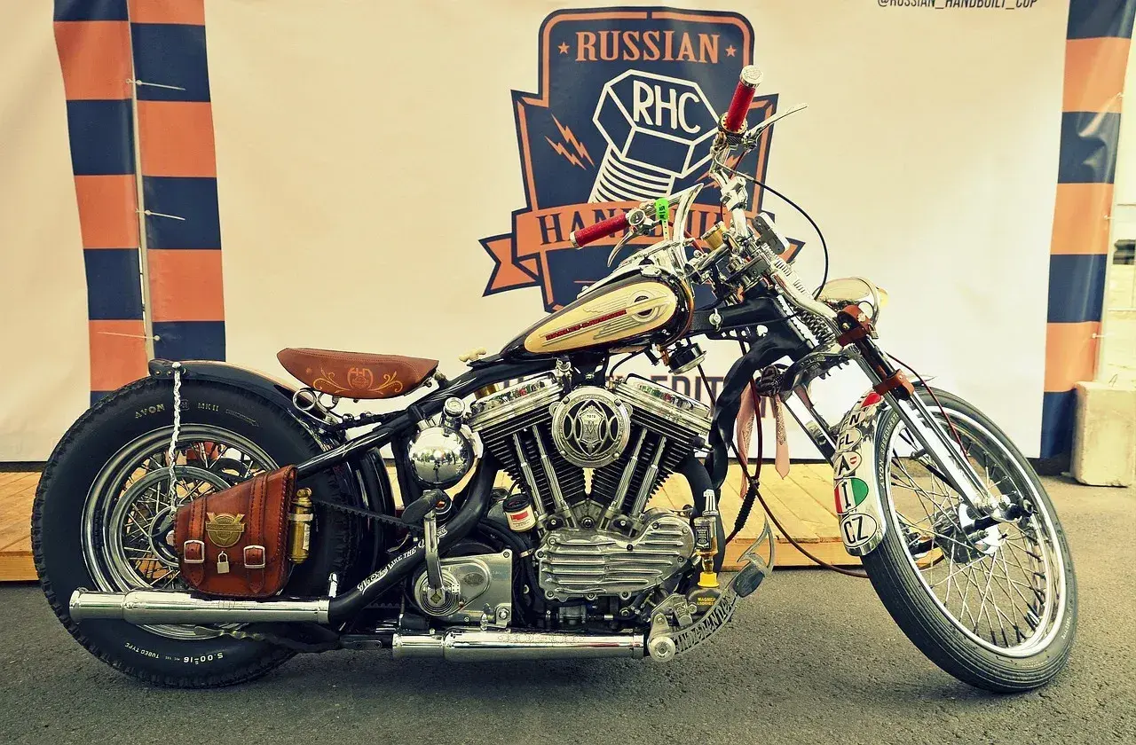 Customowy motocykl z chromowanymi elementami, skórzanym siedzeniem i sakwą, na tle baneru Russian RHC.