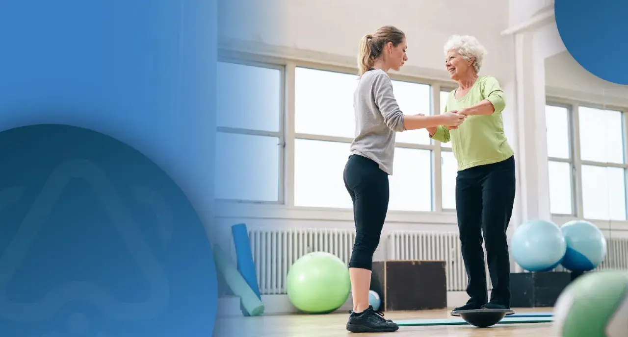 Physiotherapeutin hilft älterer Frau auf Balance Board, um Sturzgefahr zu reduzieren.