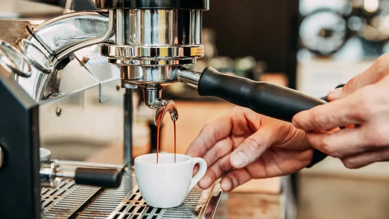 Frisch gebrühter Espresso fließt aus der Maschine in eine kleine Tasse. Die Zubereitung von handgebrühtem Kaffee ist ein Kunstwerk.