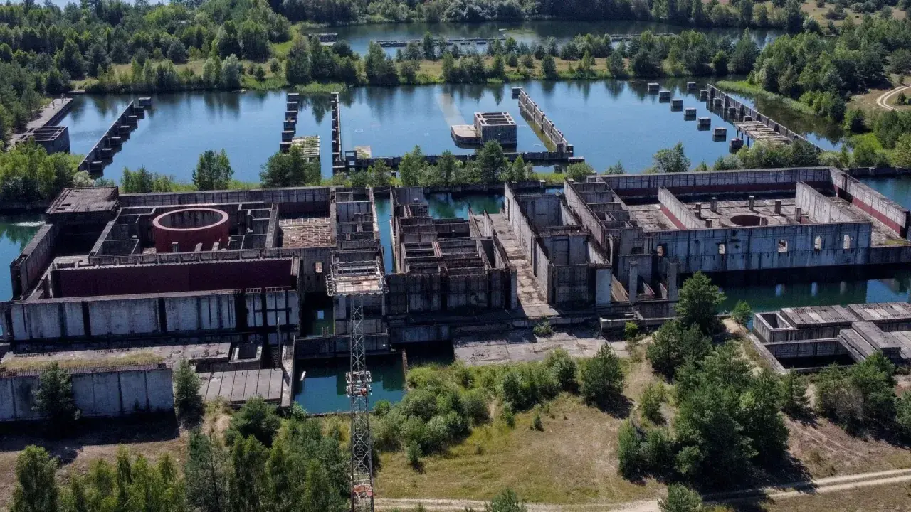 Niedokończona elektrownia w Żarnowcu, z betonowymi konstrukcjami i basenami wypełnionymi wodą, otoczona zielenią.