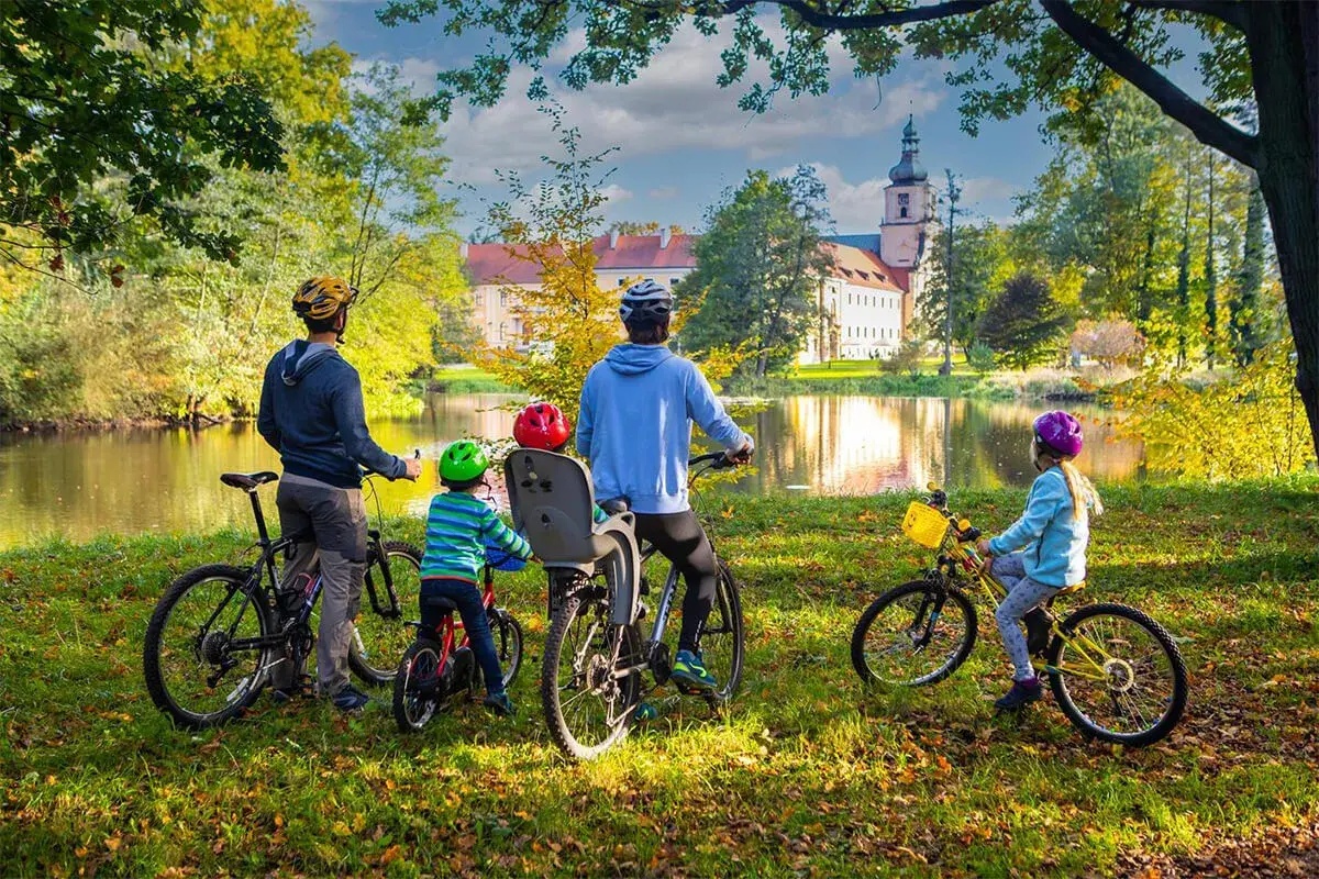 Rodzina na rowerach podziwia jesienny krajobraz krainy Górnej Odry. W tle pałac i jezioro.
