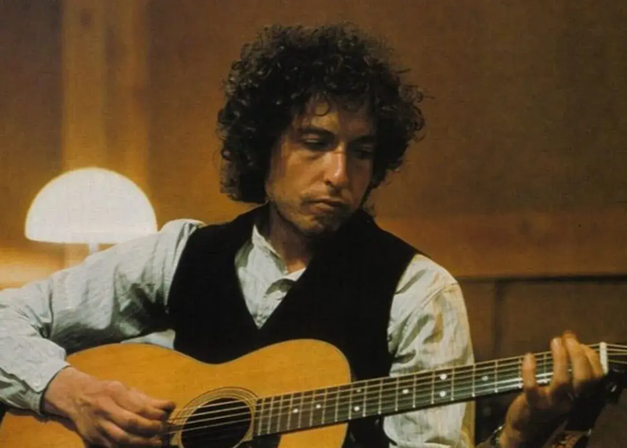 Bob Dylan gra na gitarze, tworząc ponadczasowe utwory.