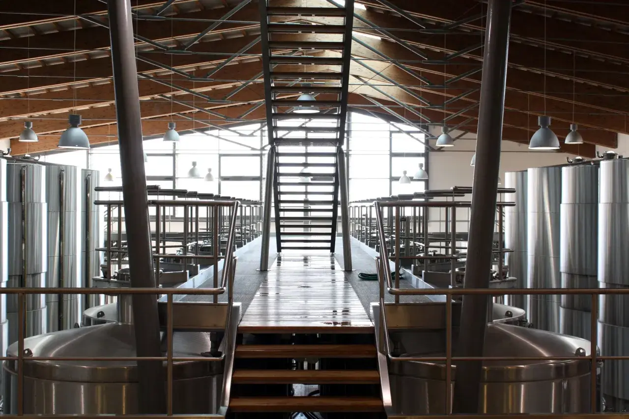 Interno di una cantina moderna con grandi serbatoi d'acciaio e una scala centrale. L'architettura ricorda un progetto di Renzo Cotarella.