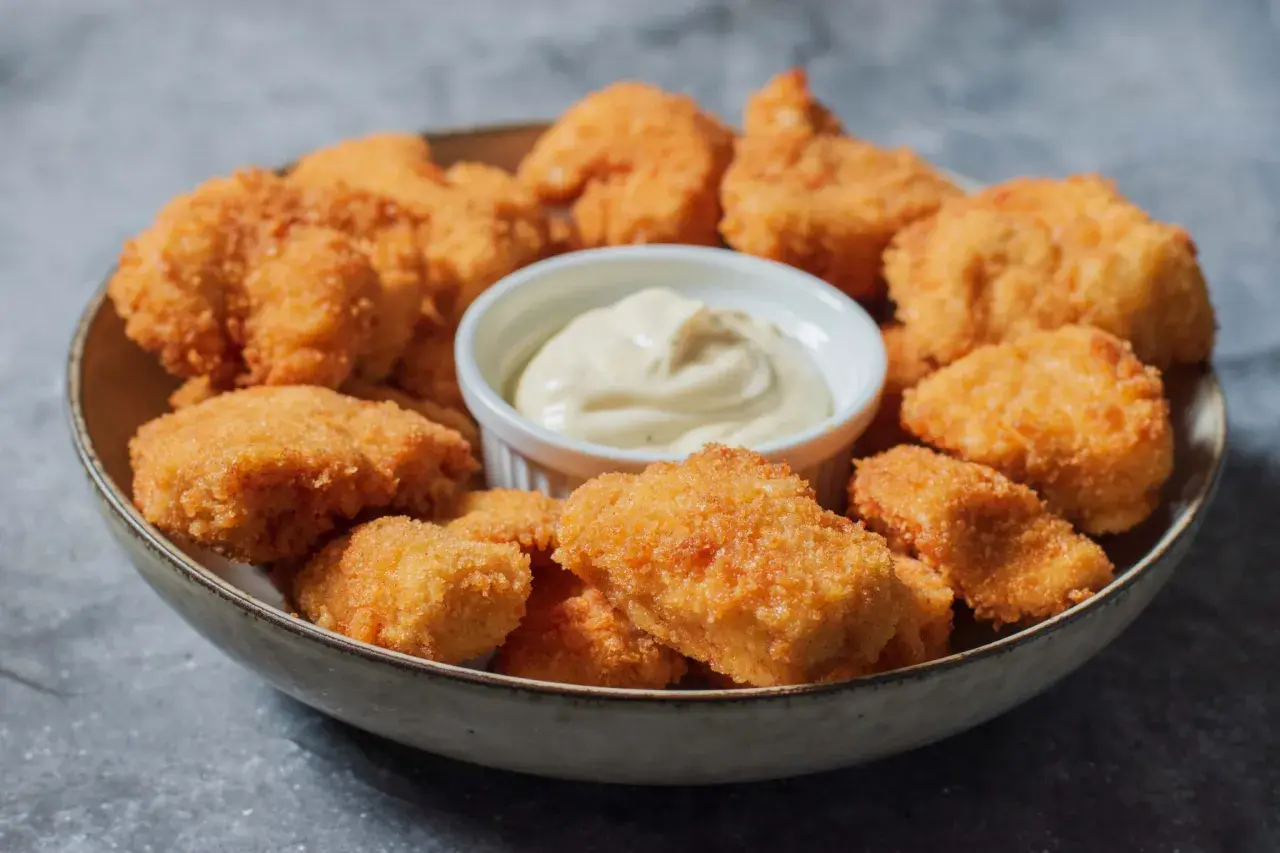 En skål med gyllene, krispiga chicken nuggets och en liten skål med krämig dipp. Perfekt för en snabb och god måltid.