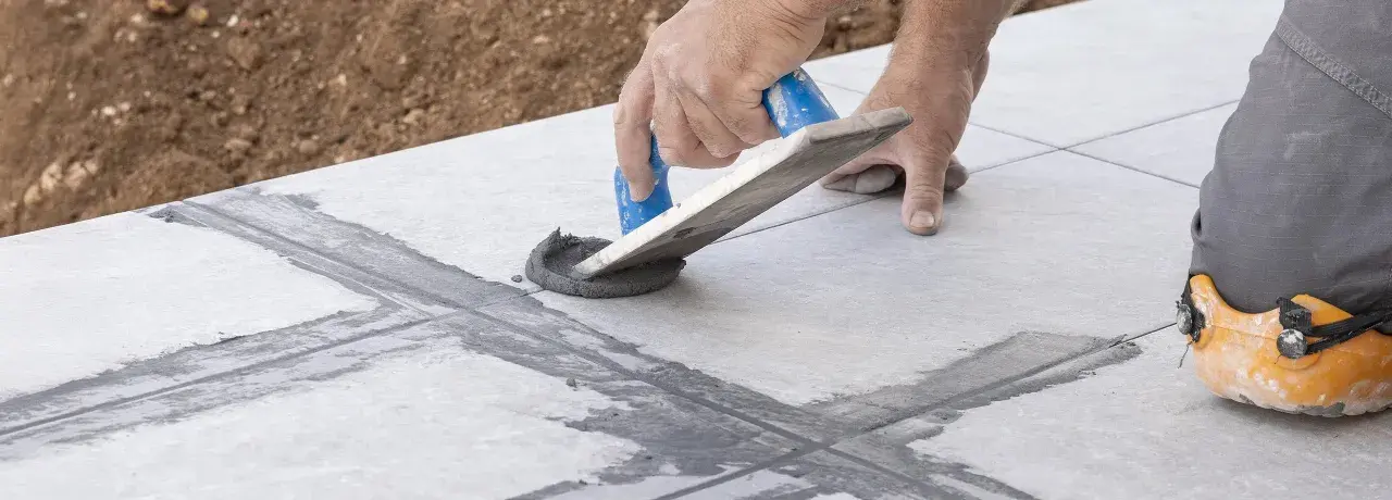Hand arbeitet mit Spachtel, um graue Masse in Fliesenfugen zu verteilen. Präzises fliesenfugen abdichten für ein perfektes Ergebnis.