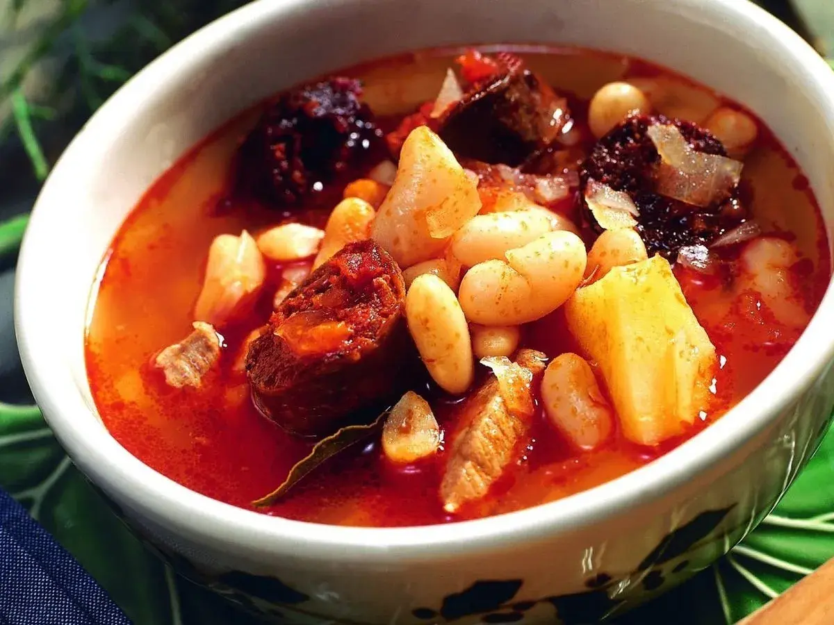 Un reconfortante plato de alubias con chorizo, trozos de patata y carne en un caldo rojizo.