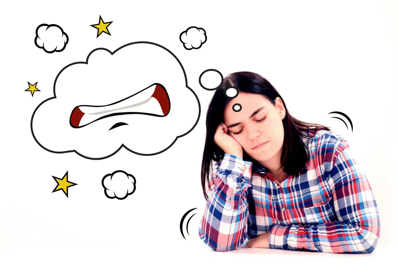 Mujer dormida con un globo de pensamiento que muestra una boca enfadada, como si soñara que se le cae una muela.