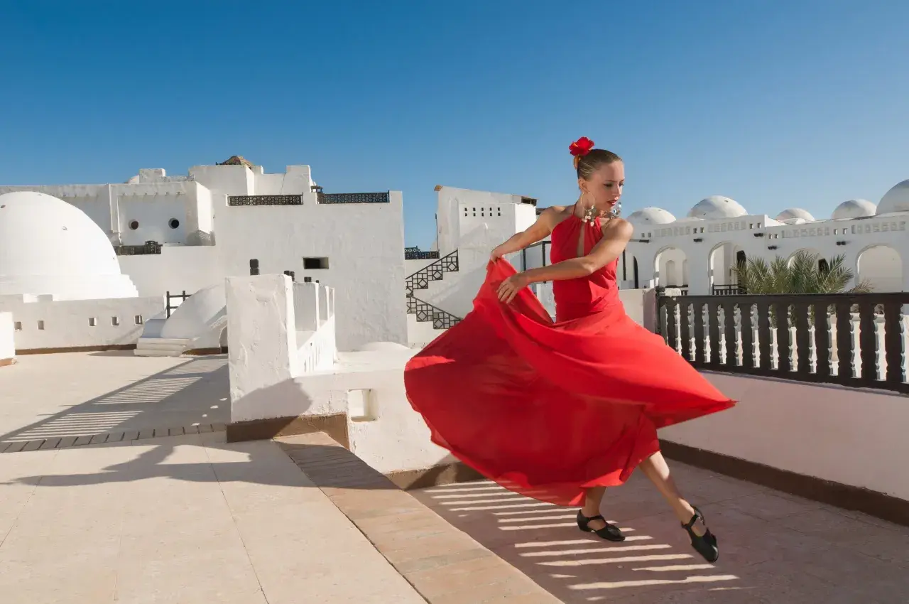 Bailarina con vestido rojo gira con gracia, evocando la pasión de los flamencos de Jerez bajo un cielo azul.