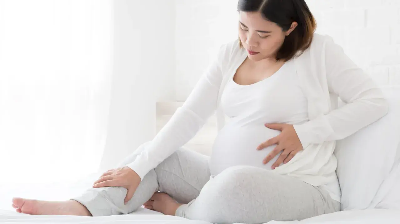 Schwangere Frau mit Hand auf dem Bauch und Bein, die Beschwerden oder Kompression während der Schwangerschaft andeutet.