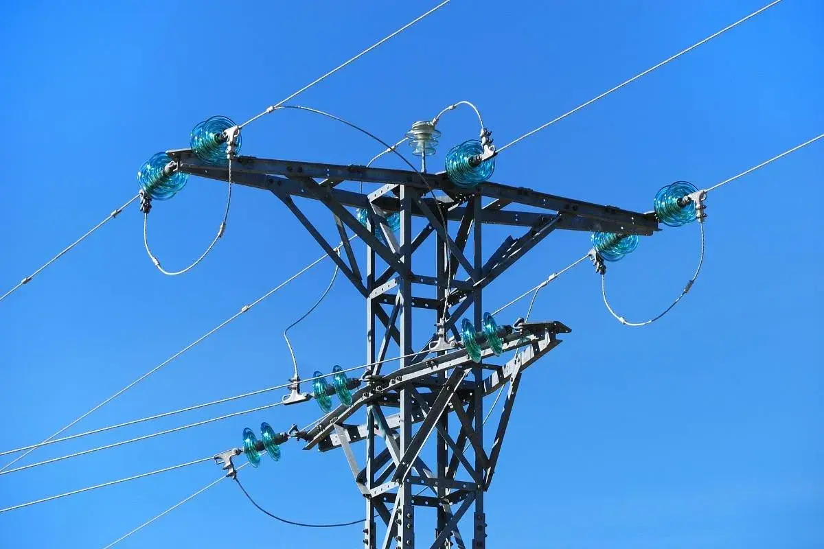 Metalowa konstrukcja słupa energetycznego z niebieskimi izolatorami, przez które biegnie linia średniego napięcia.