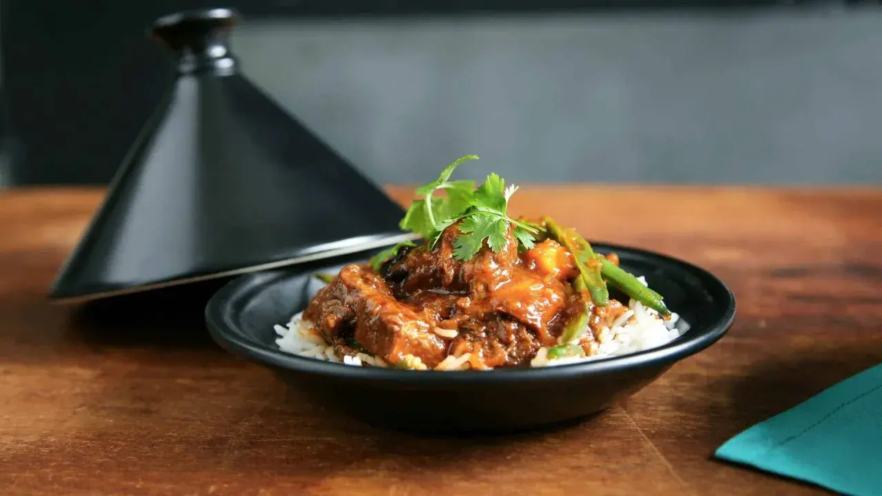 Un plat de riz blanc garni d'un ragoût de bœuf savoureux, aux haricots verts et coriandre, servi à côté d'un tajine noir. La marinade boeuf a conféré une sauce riche et appétissante.