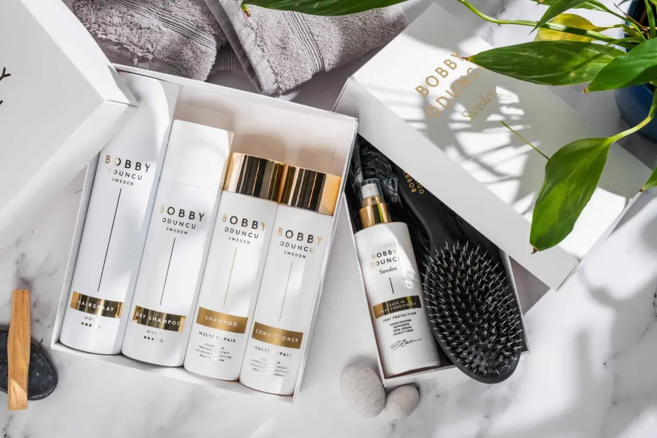 En presentbox med Bobby Oduncu-produkter för att ta hand om håret: hårspray, torrschampo, schampo, balsam och leave-in spray. En borste ligger bredvid.