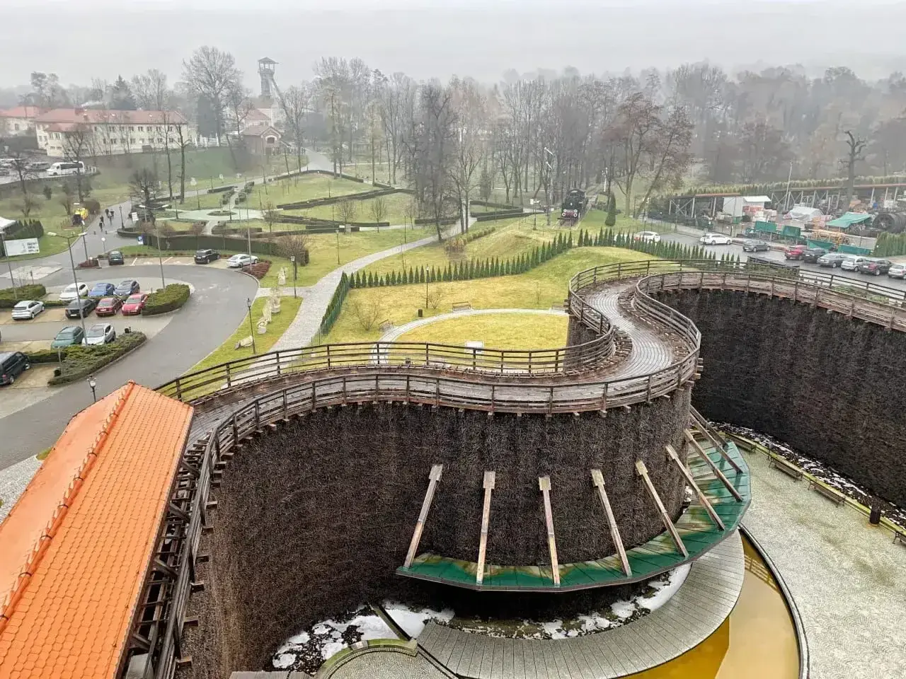 Wieliczka miasto. Drewniane tężnie solankowe tworzą malowniczą spiralę, a w tle widać zabudowania i park.