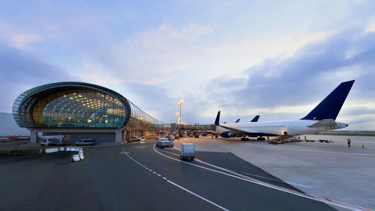 Flugzeuge am Flughafen Paris warten auf den Abflug. Ein modernes Terminalgebäude mit Glasfassade spiegelt den Himmel.