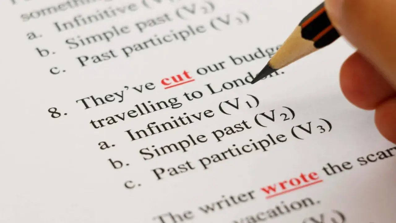 Matita evidenzia "cut" e "wrote" su un foglio con esercizi di grammatica inglese, tra cui la forma infinito.